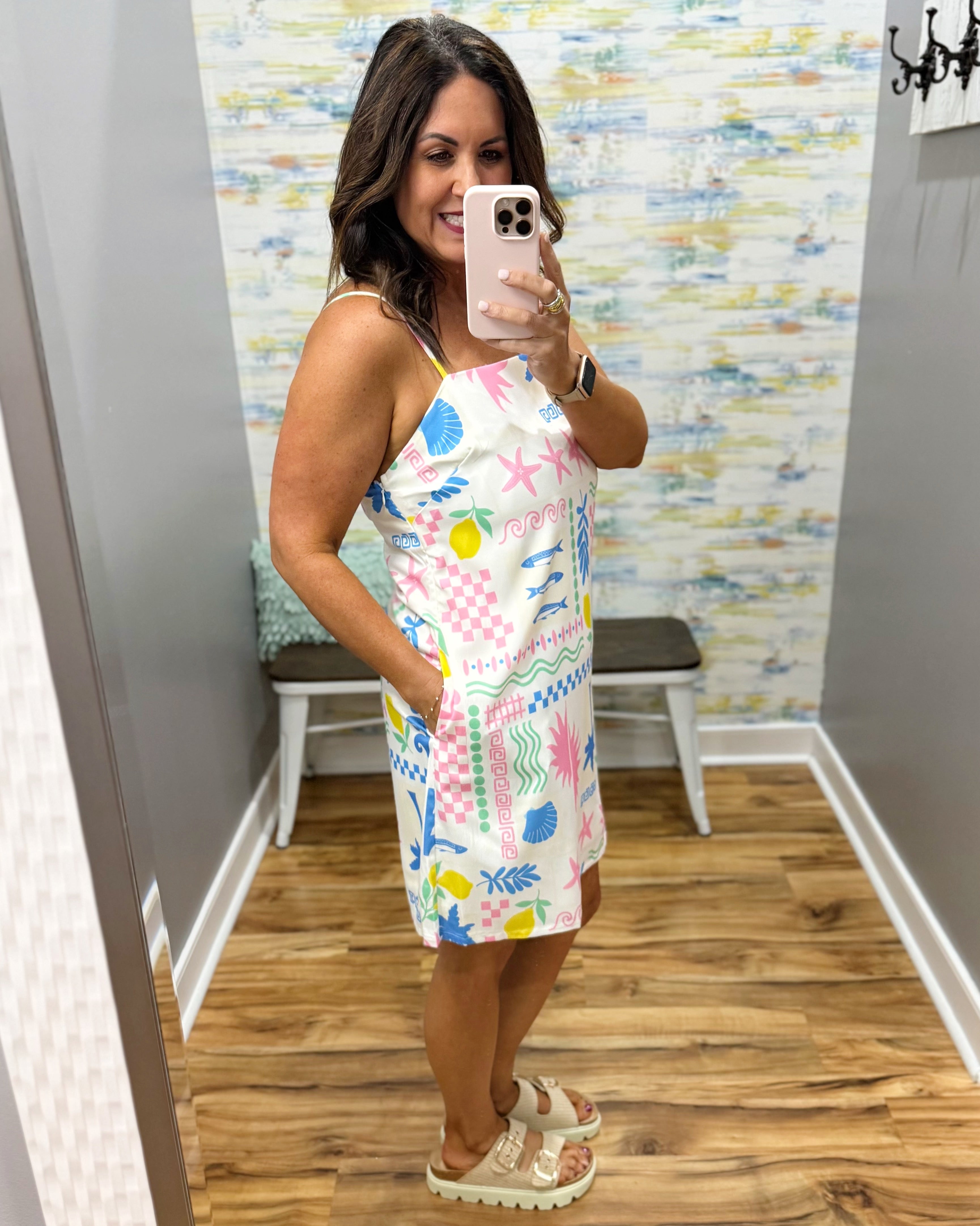 Woman taking a mirror selfie wearing a colorful dress in a room with a patterned wall.