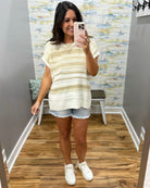 Woman taking a mirror selfie wearing a striped shirt and denim shorts in a room with a patterned wall.
