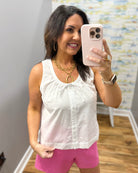 Woman wearing a white sleeveless top and pink shorts.