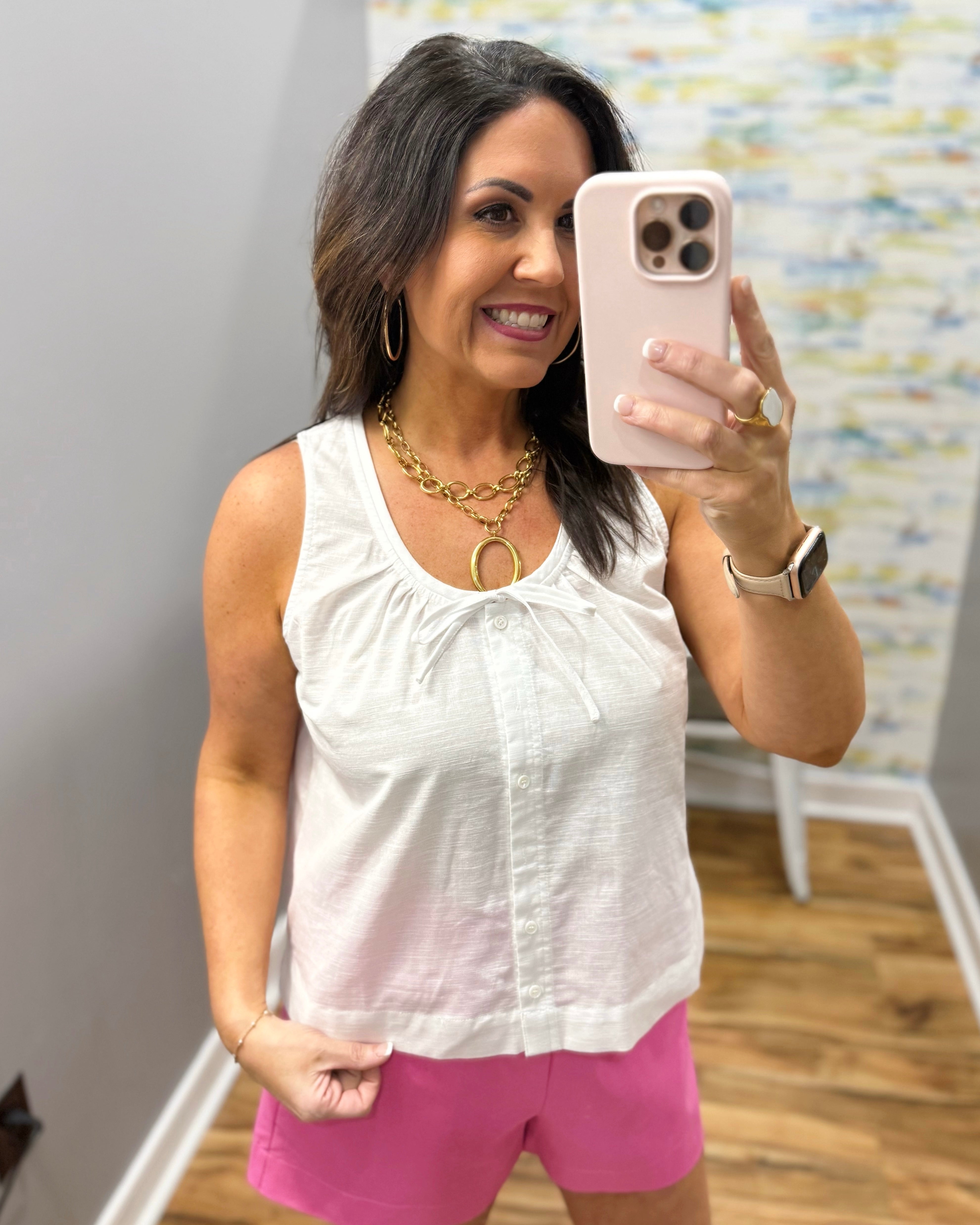 Woman wearing a white sleeveless top and pink shorts.