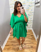 Woman wearing a green dress taking a mirror selfie in a store.