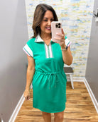 Woman taking a mirror selfie wearing a green dress with white and pink accents.