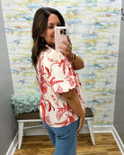 Woman taking a mirror selfie wearing a red floral shirt and blue jeans in a room with colorful wall art.