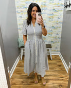 Woman wearing a black and white striped dress in a room with patterned wallpaper.