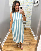 Woman taking a mirror selfie wearing a blue and white striped dress in a room with wooden flooring and a textured wall.