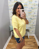 Woman taking a mirror selfie wearing a yellow top and denim shorts in a room with a colorful wall.