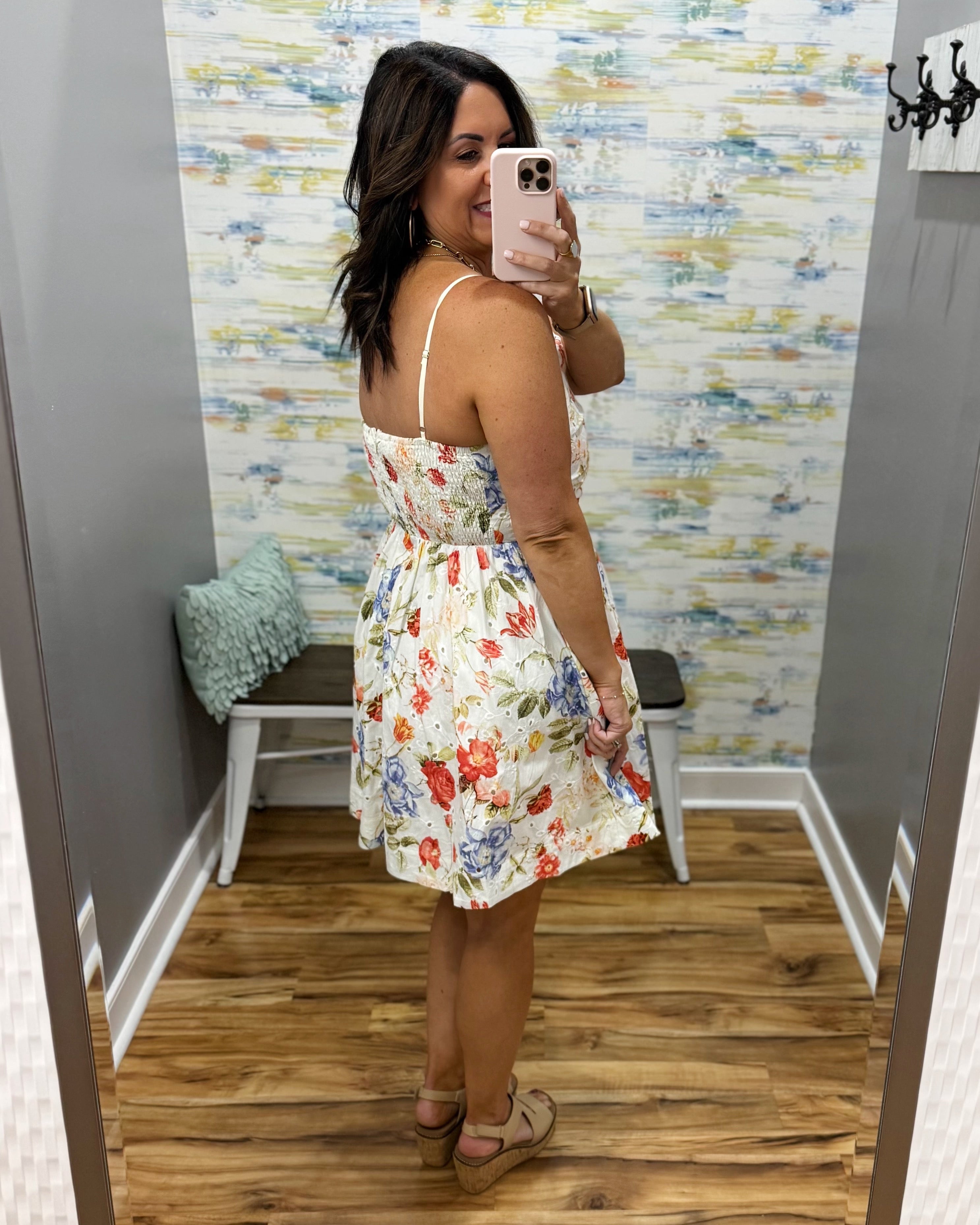Woman taking a mirror selfie wearing a floral dress in a room with a colorful wall.