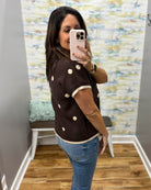 A woman takes a mirror selfie wearing a dark brown short-sleeve knit top with cream-colored polka dots and trim, paired with blue jeans in a fitting room.