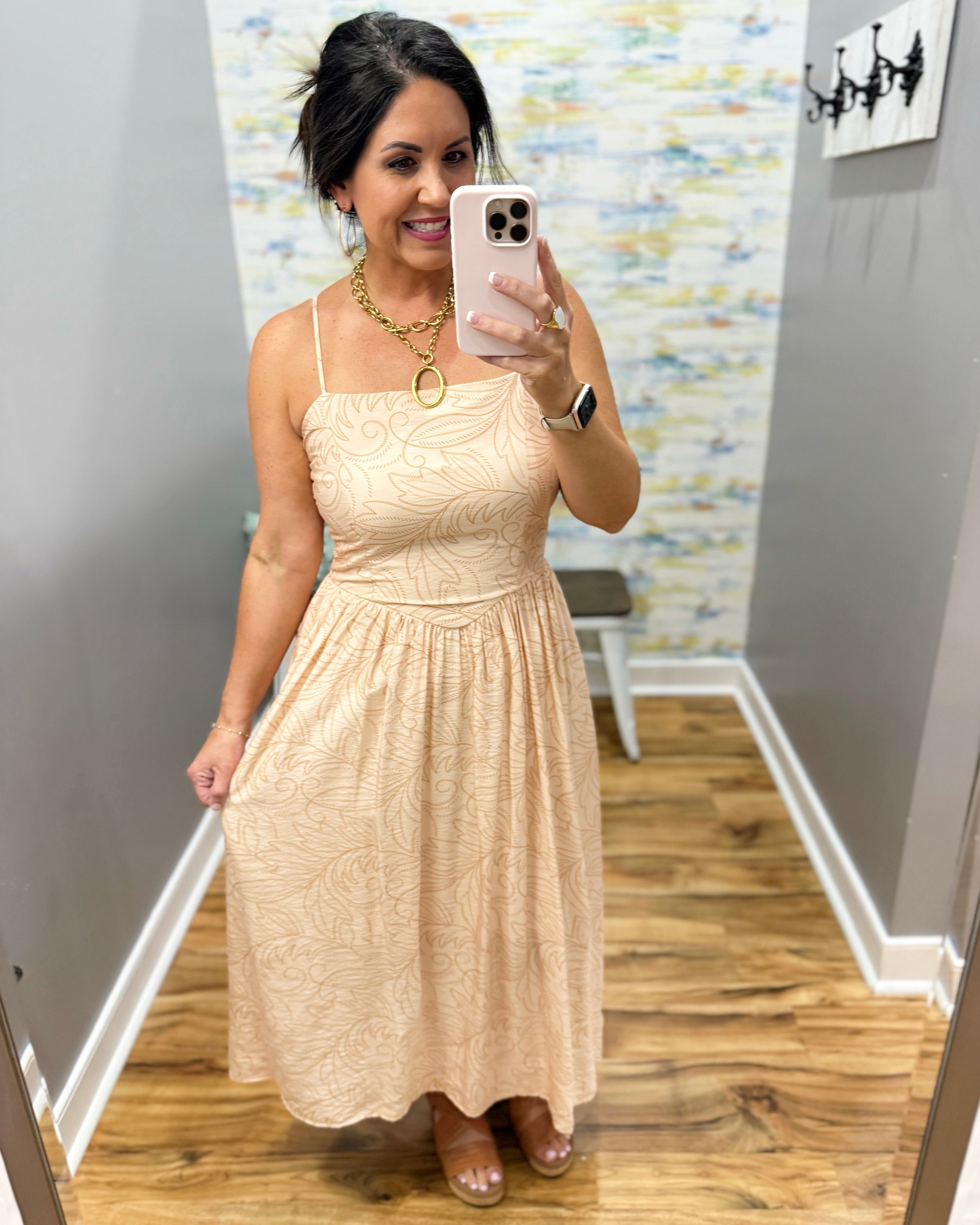 Woman taking a mirror selfie wearing a beige dress in a room with a colorful wall.