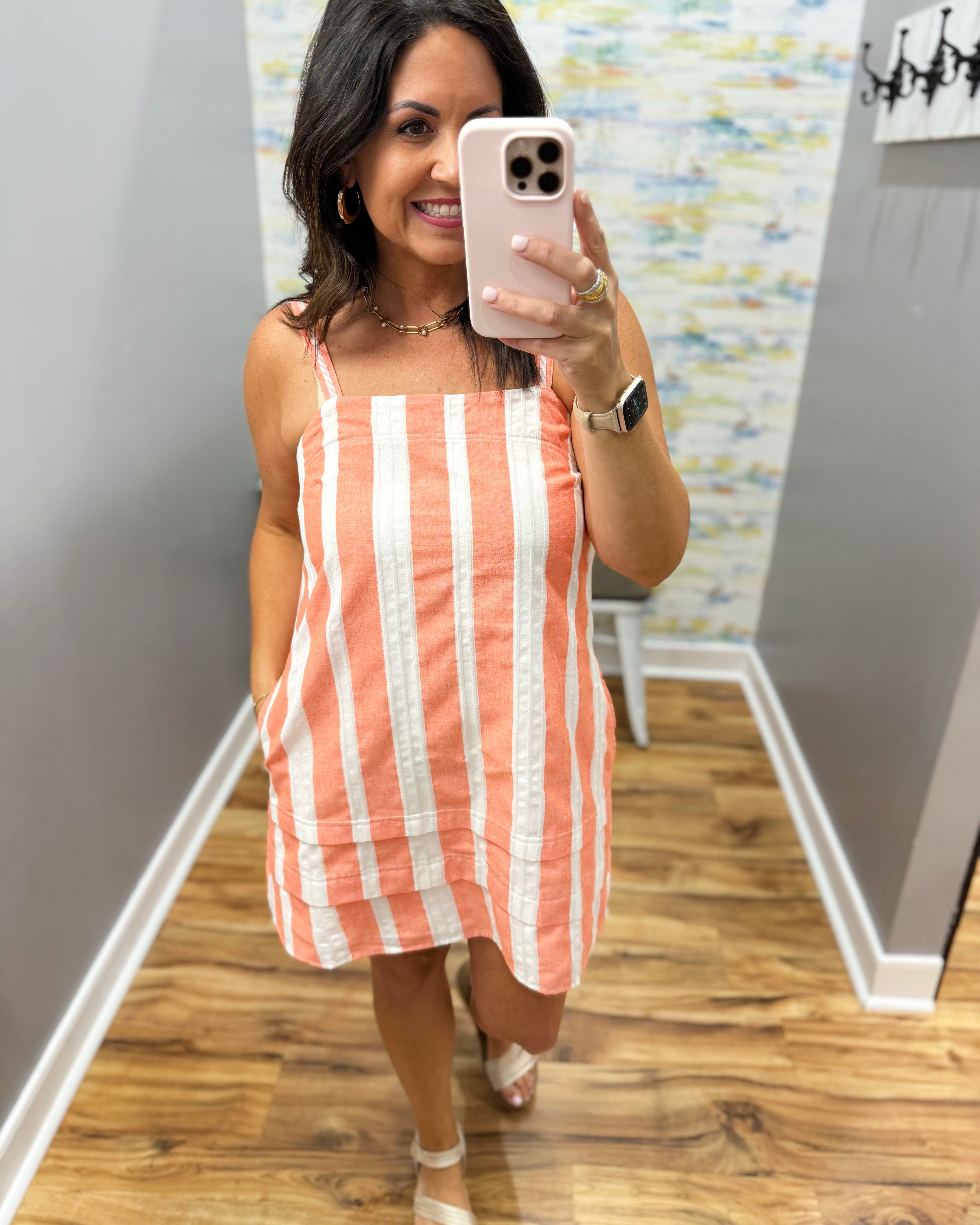 Woman taking a mirror selfie wearing a striped dress in a room with a colorful wall.
