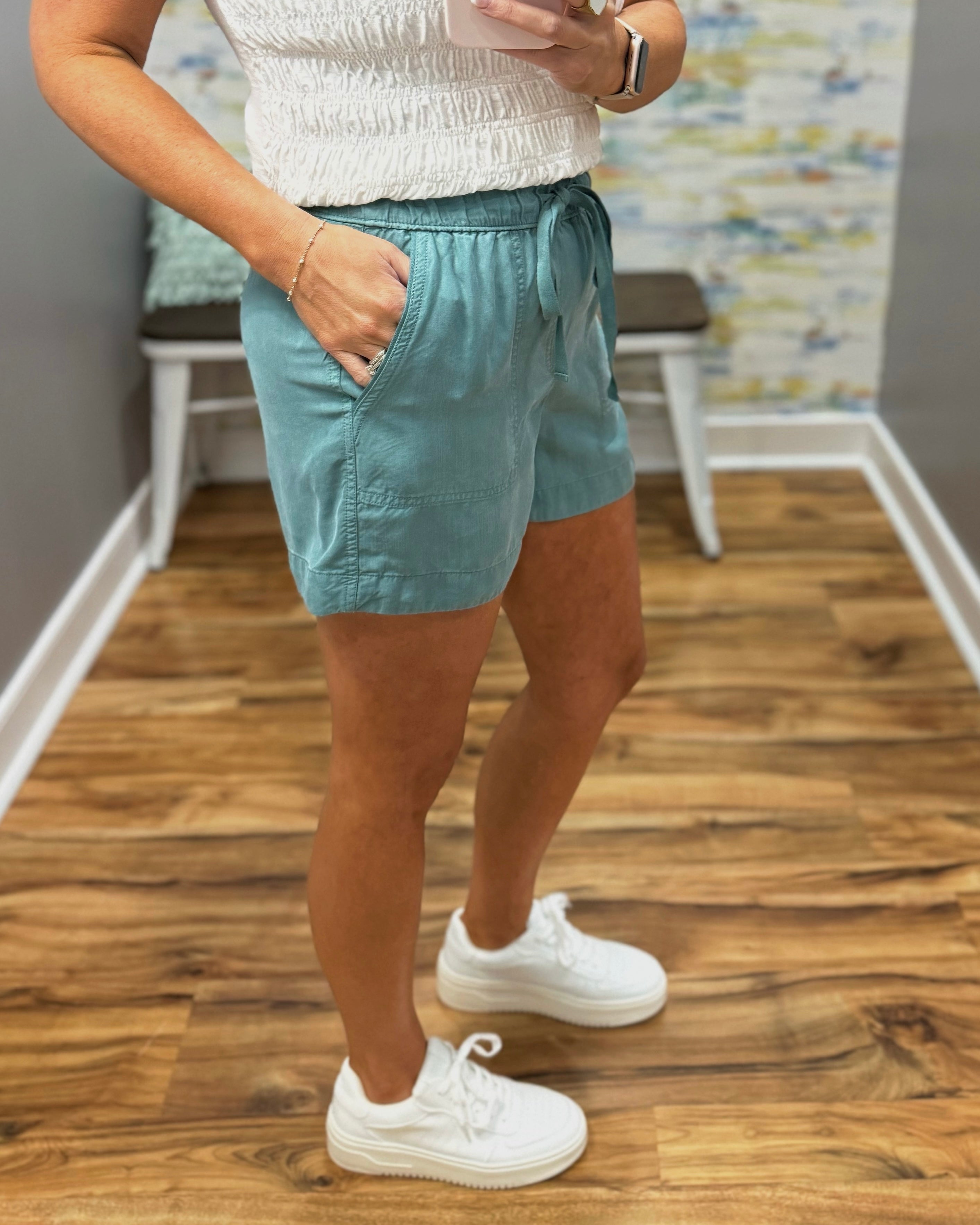 Person wearing light blue shorts and white sneakers on a wooden floor.