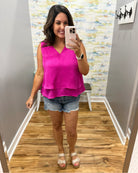 Woman taking a mirror selfie wearing a pink top and denim shorts in a room with patterned wallpaper.