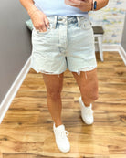 Person wearing light denim shorts and white sneakers on a wooden floor.