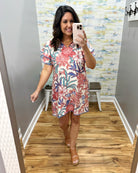 Woman taking a mirror selfie wearing a floral dress in a room with a colorful wall.