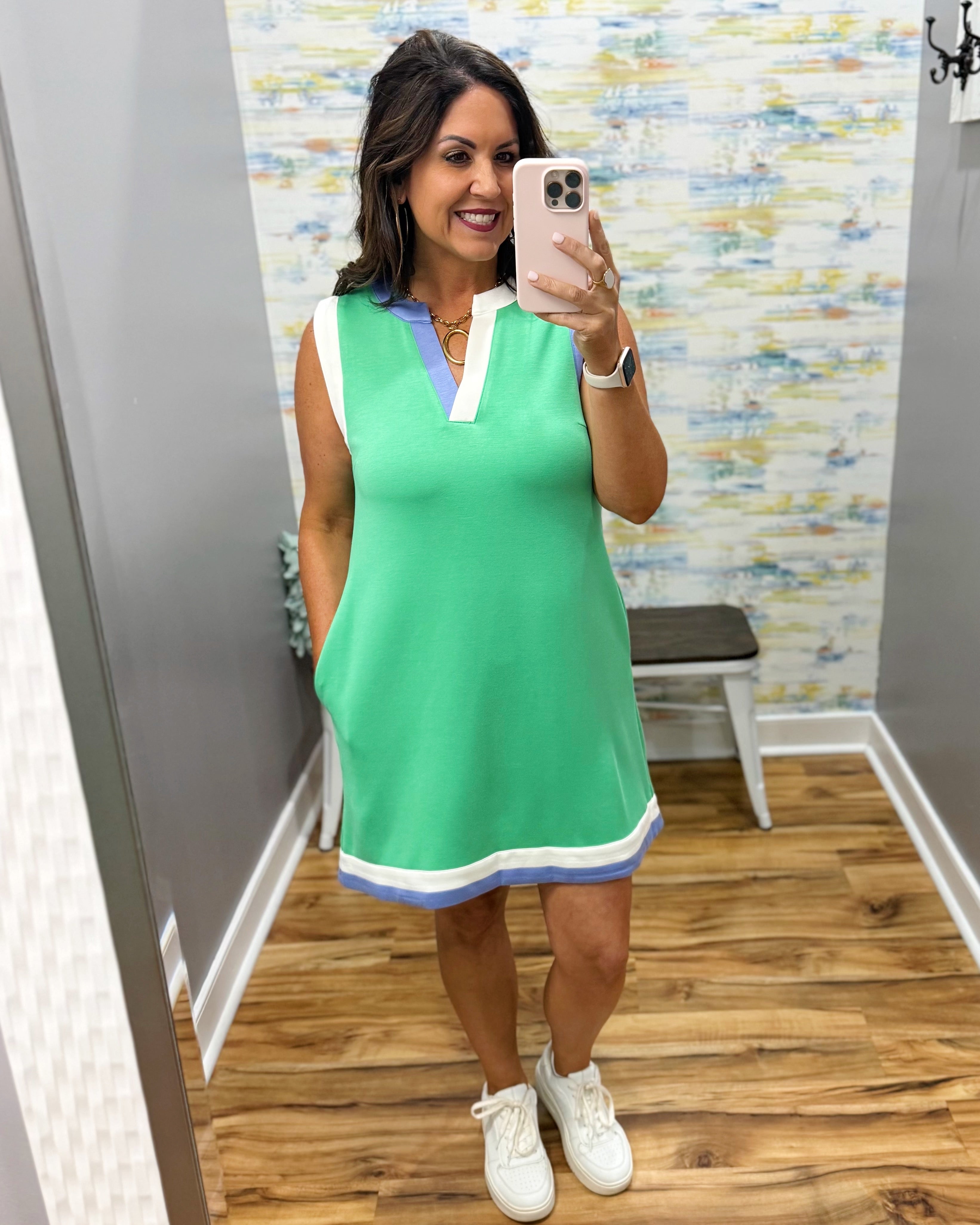 Woman taking a mirror selfie wearing a green dress with white accents.