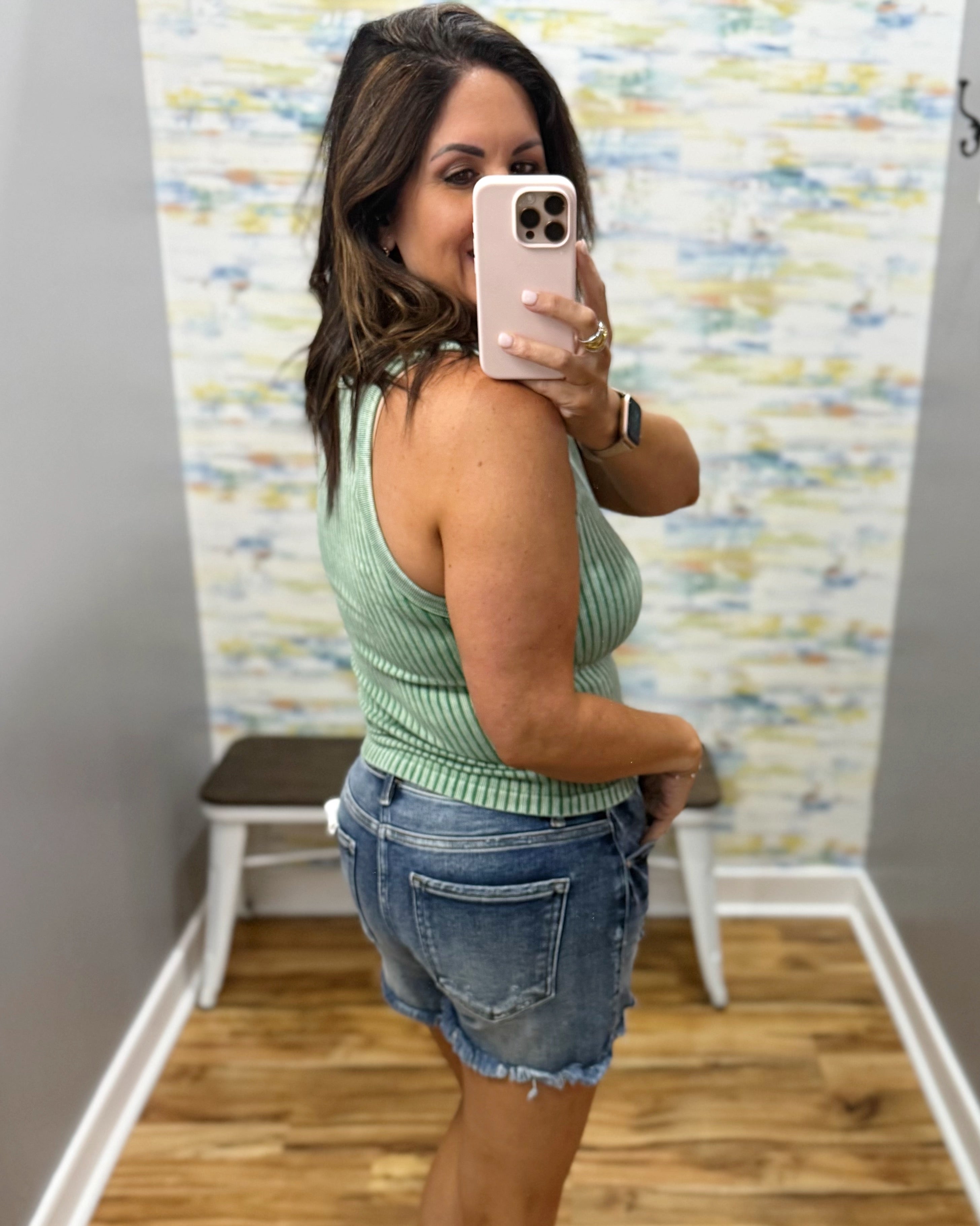 woman wearing dark green tank with denim shorts.