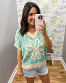 Woman taking a mirror selfie wearing a light green crochet top with a floral design.
