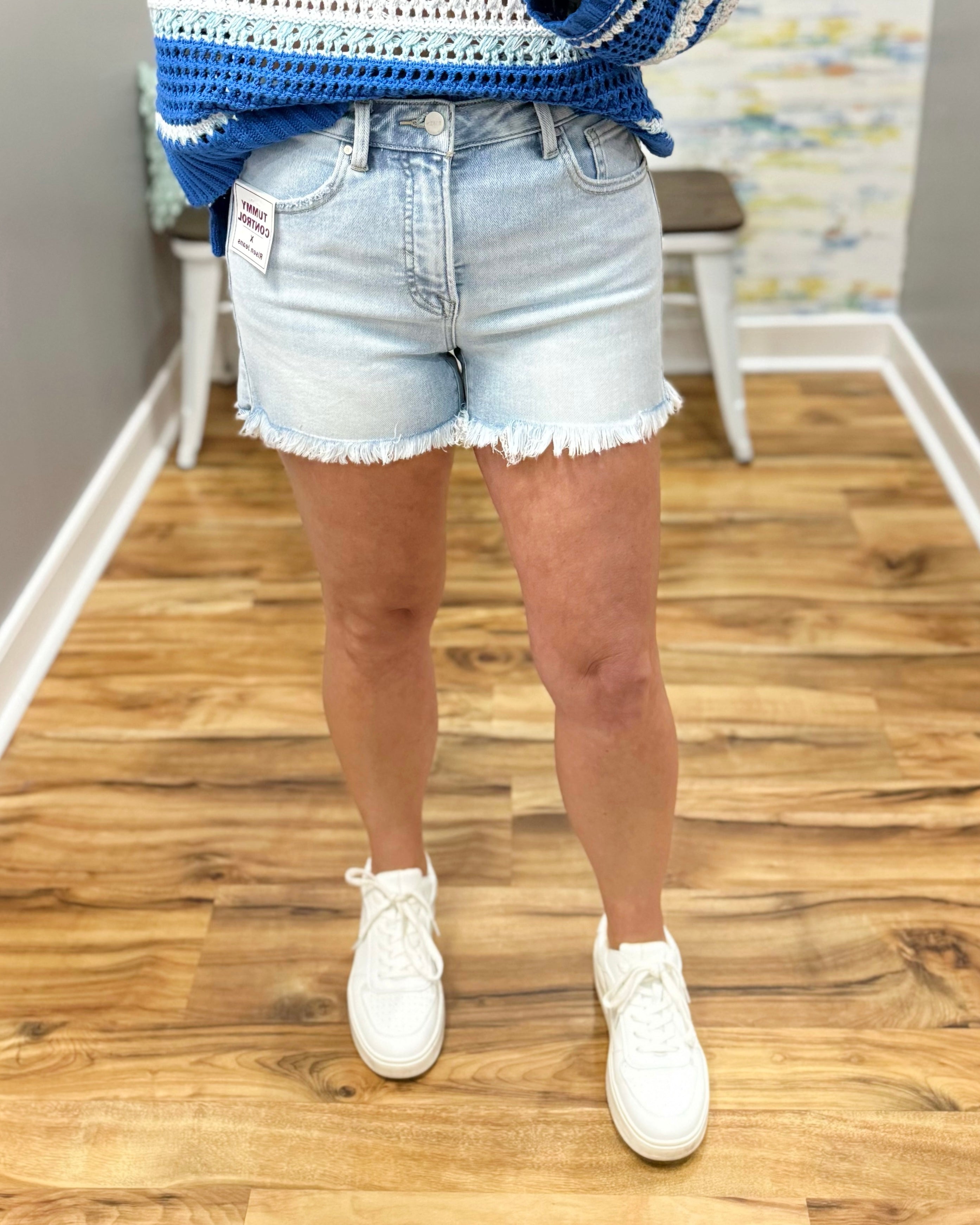 Person wearing light blue denim shorts and white sneakers on a wooden floor.