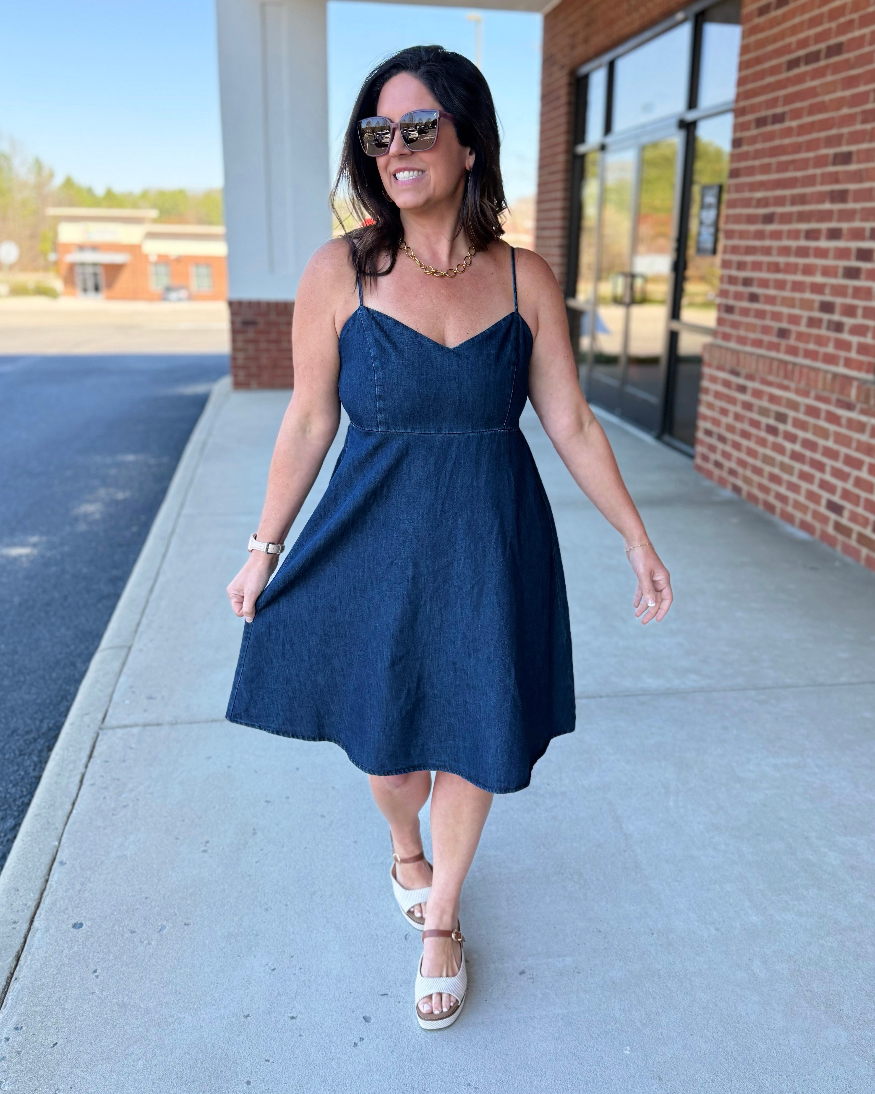 Woman in a blue dress walking on a sidewalk with a building in the background
