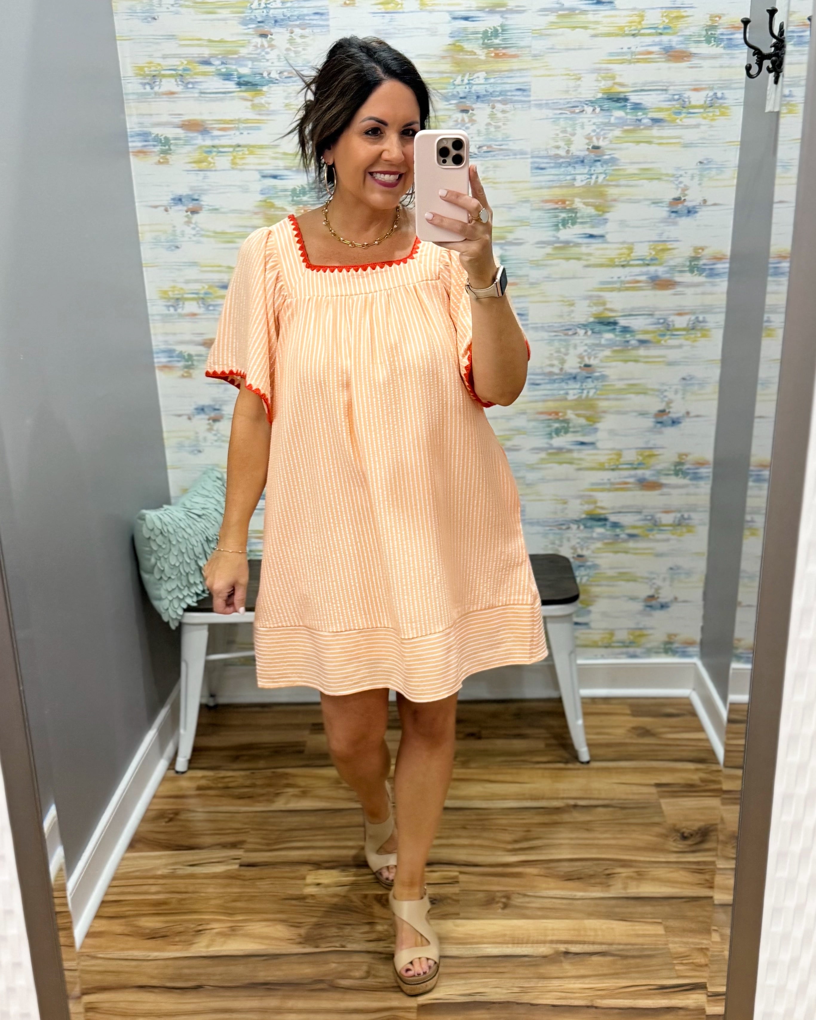 Woman taking a mirror selfie wearing an orange dress in a room with a colorful wall.