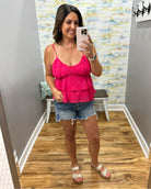 Woman taking a mirror selfie wearing a pink top and denim shorts in a room with patterned wallpaper.