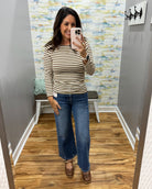A woman takes a mirror selfie in a fitting room wearing a beige and brown horizontally striped long-sleeve top with wide-leg blue jeans and brown Mary Jane shoes.