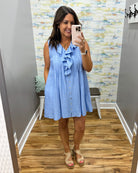 Woman wearing a blue dress taking a mirror selfie in a room with a patterned wall.
