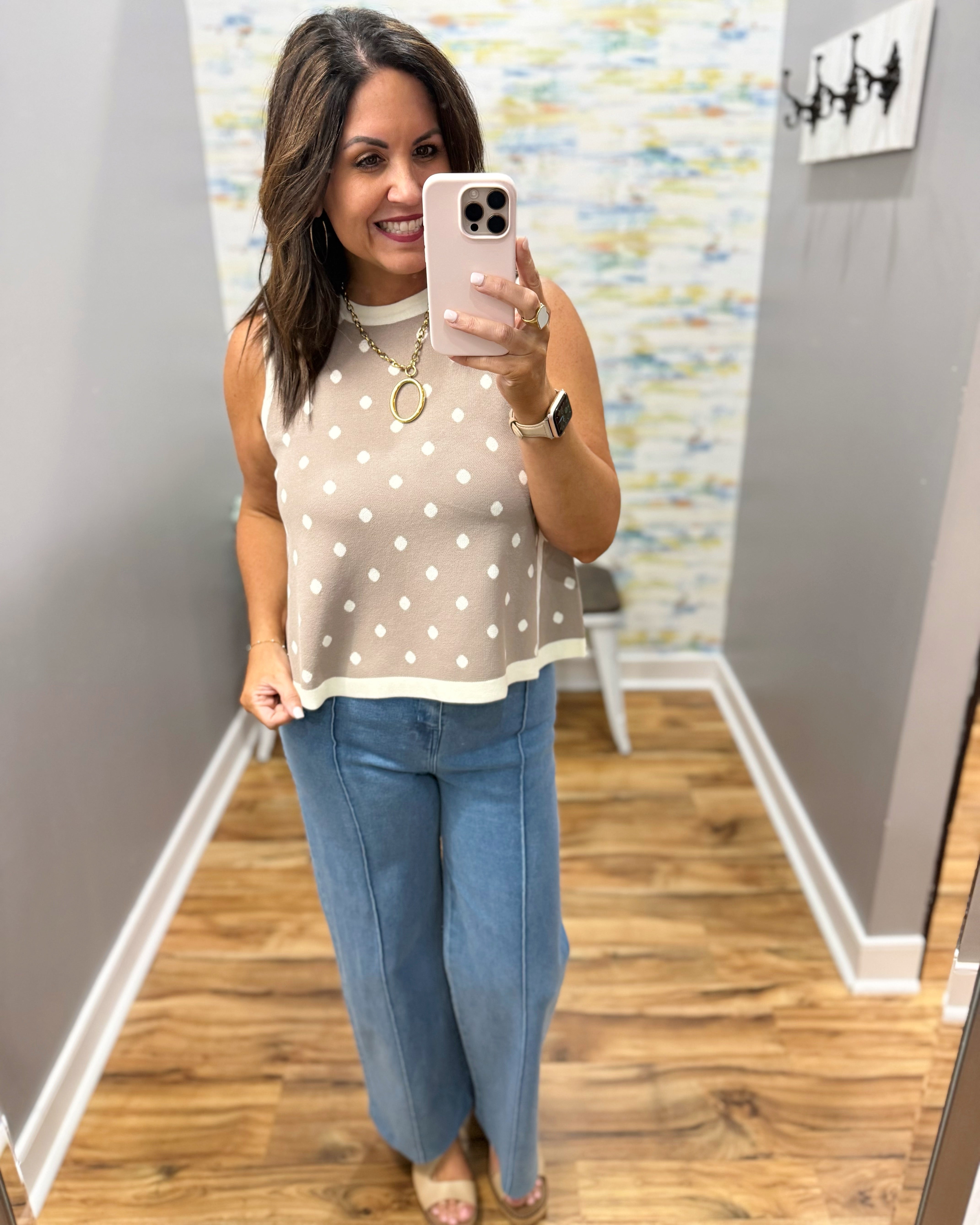 Woman taking a mirror selfie wearing a polka dot top and jeans in a room with a colorful wall.