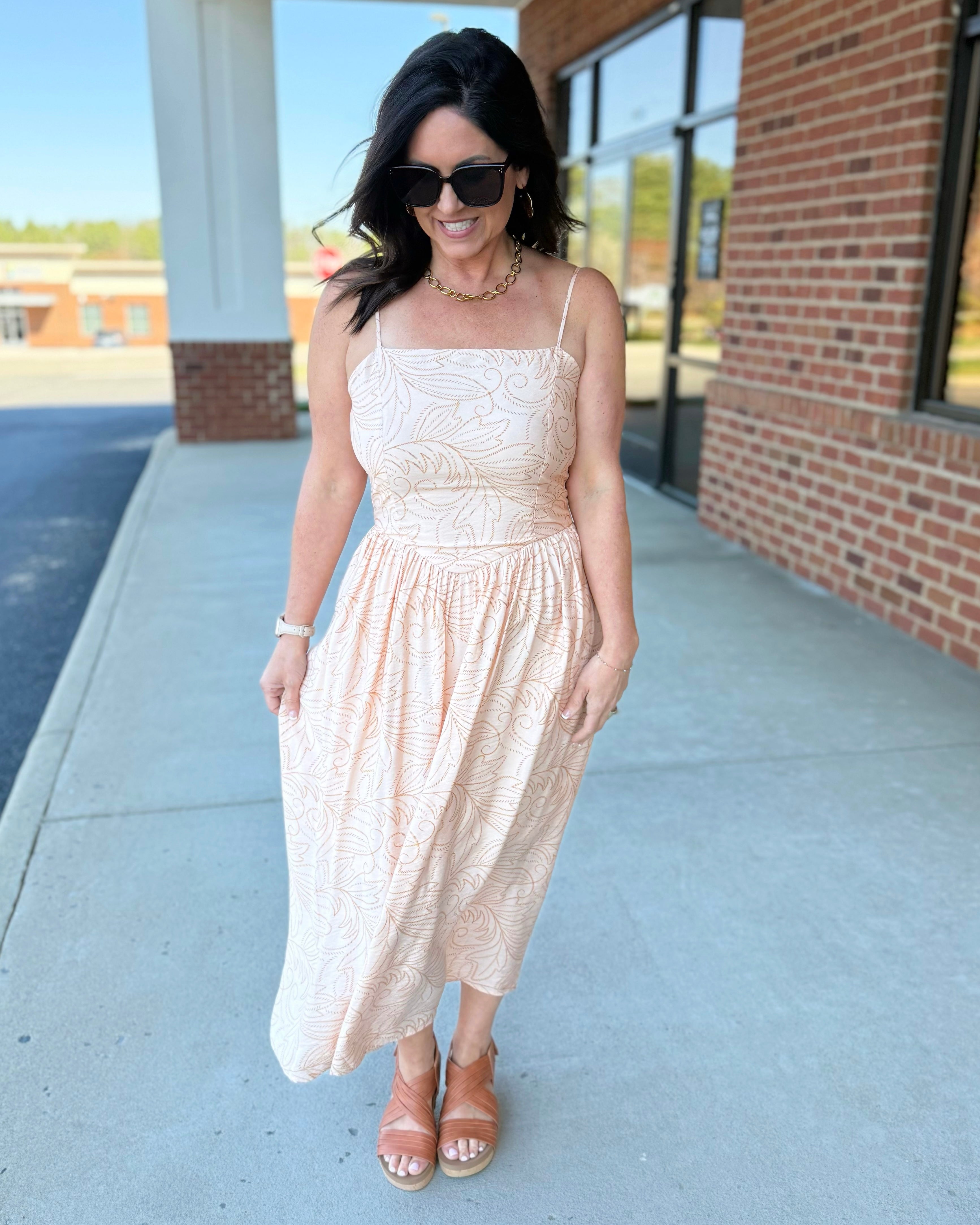 Woman in a beige dress standing on a sidewalk with a building in the background