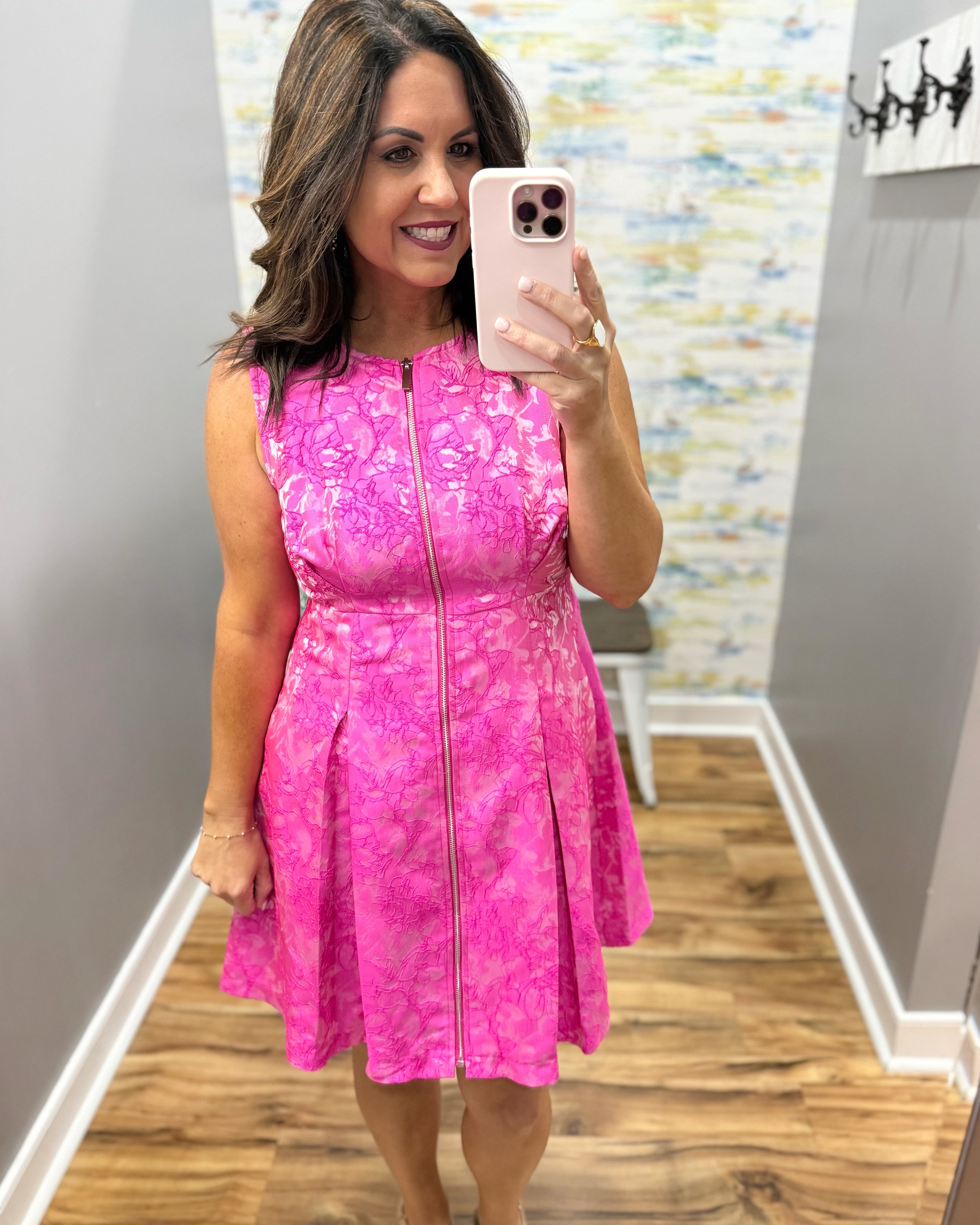 Woman taking a mirror selfie wearing a pink dress with a pattern.