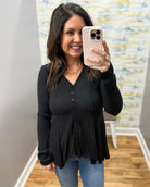 Woman taking a mirror selfie wearing a black long-sleeve top and blue jeans, holding a phone.