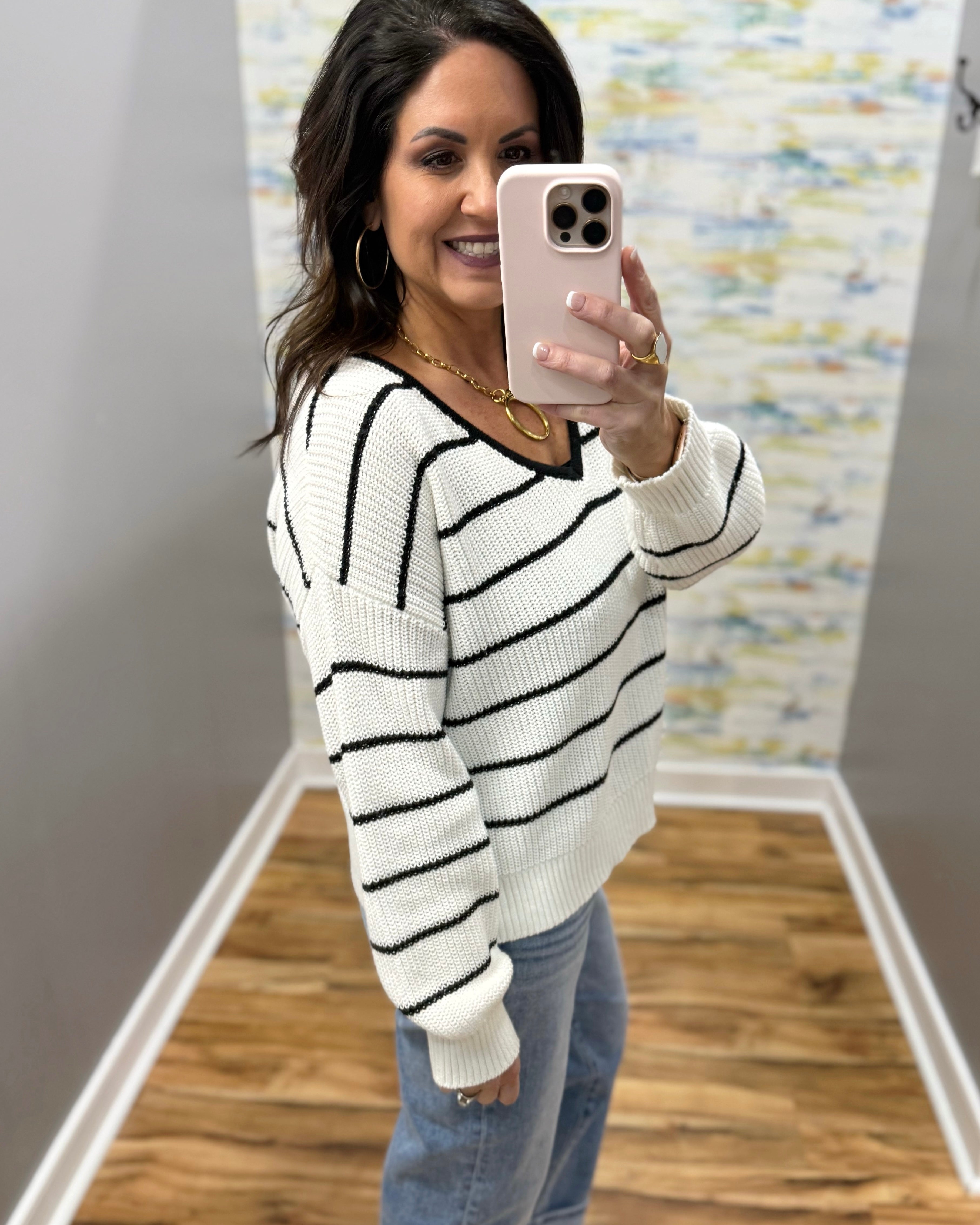 Woman taking a mirror selfie wearing a black and white striped sweater and blue jeans.