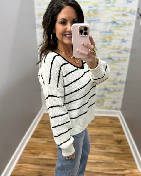 Woman taking a mirror selfie wearing a black and white striped sweater and blue jeans.