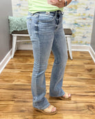 Person wearing light blue jeans standing on a wooden floor with a colorful wall in the background.