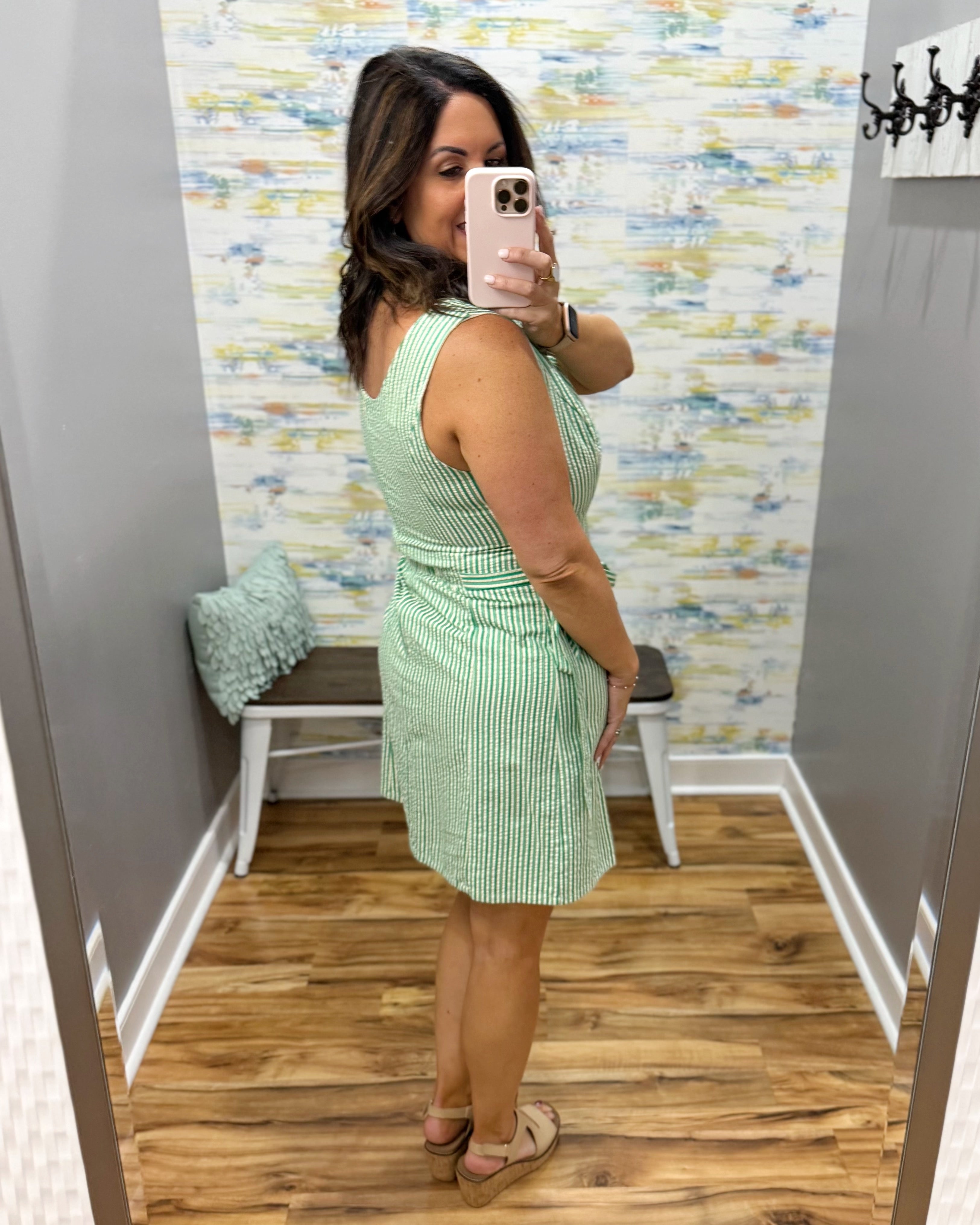 Woman taking a mirror selfie wearing a green dress in a room with patterned wallpaper.