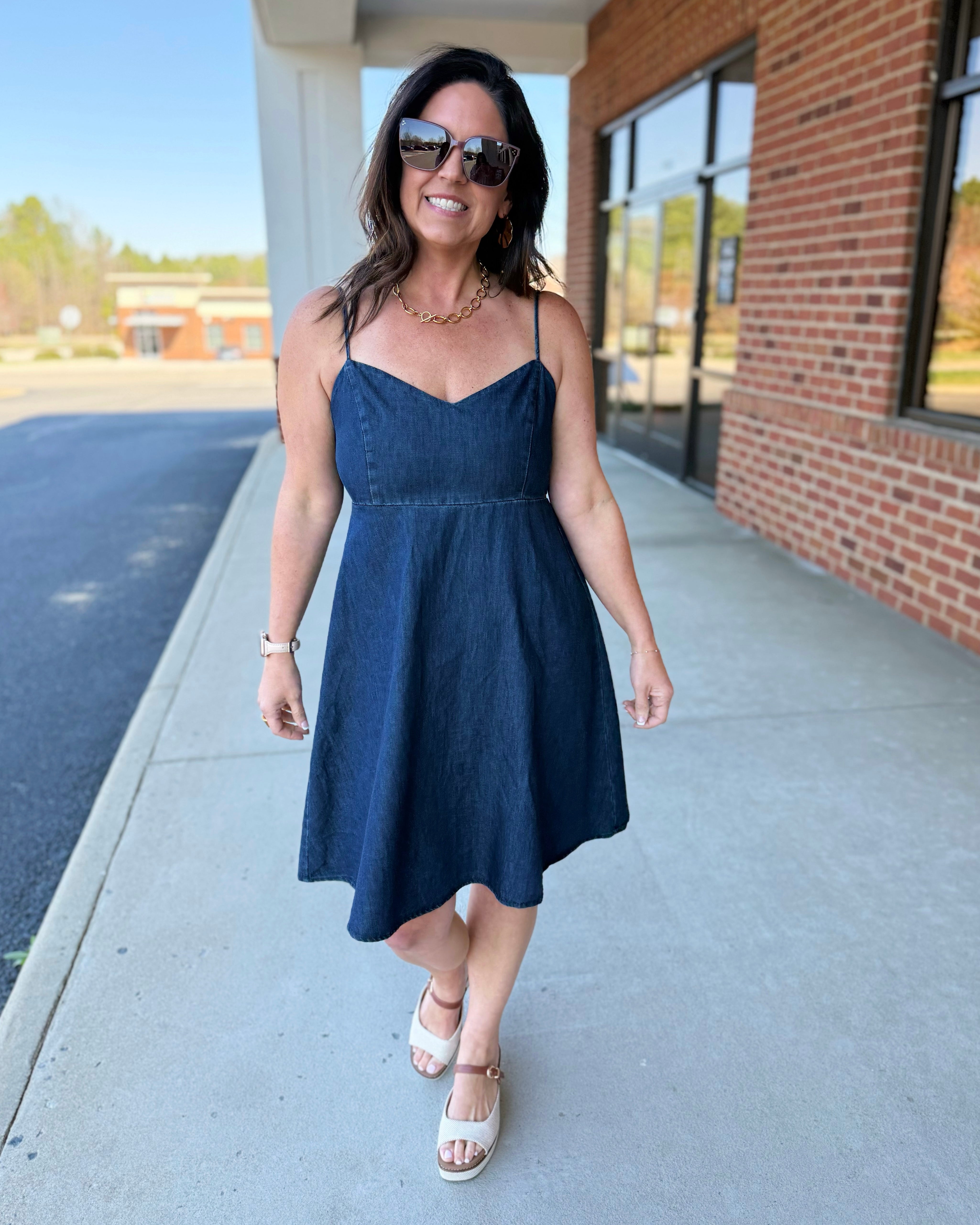 Woman in a navy dress standing on a sidewalk with a building in the background