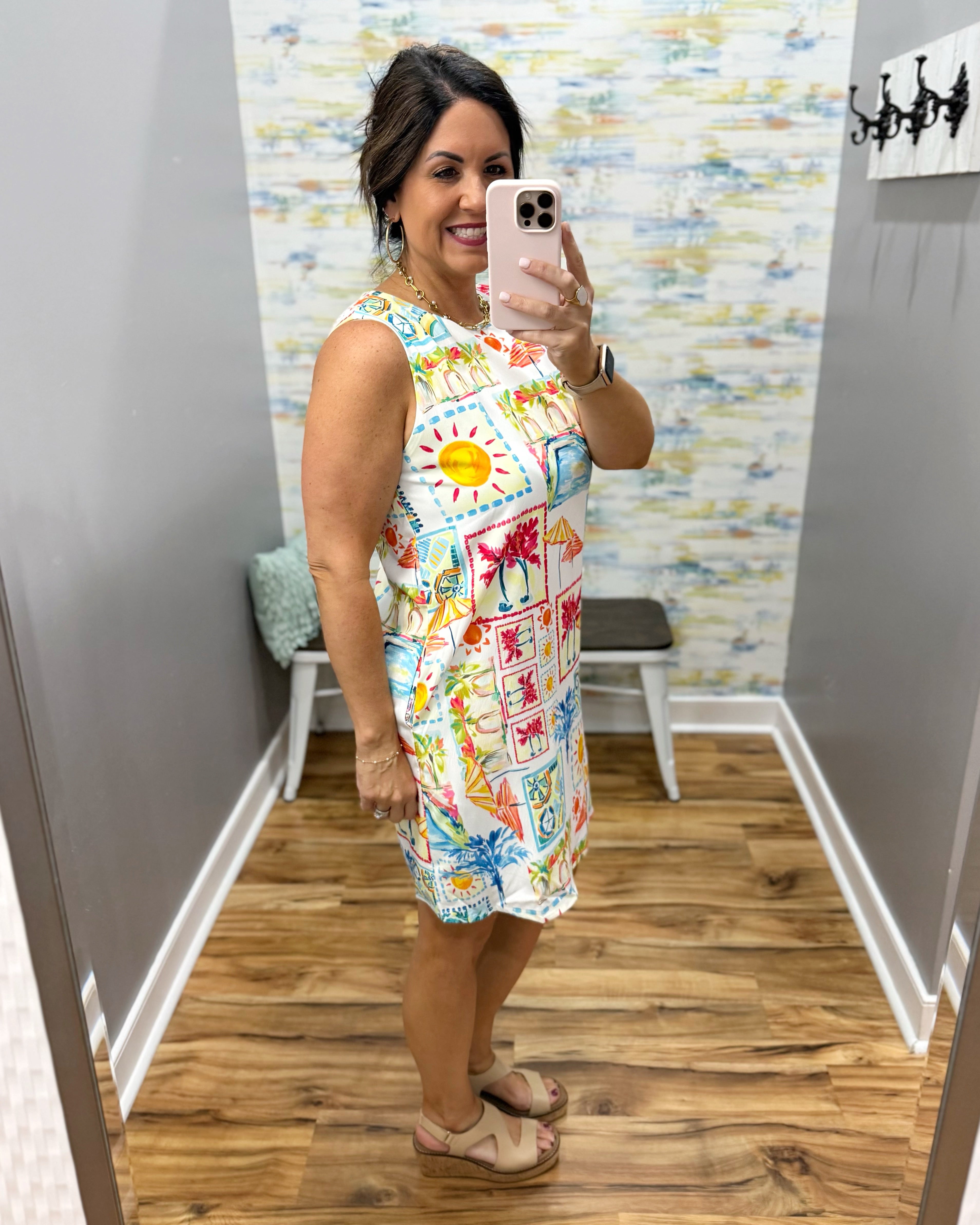 Woman taking a mirror selfie wearing a colorful dress with a pattern of suns and flowers.
