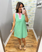 Woman taking a mirror selfie wearing a green and pink checkered dress in a room with a patterned wall.