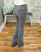 A person shown from the back wearing gray flared jeans and a white top, standing on a wood floor in front of a bench and patterned wall.