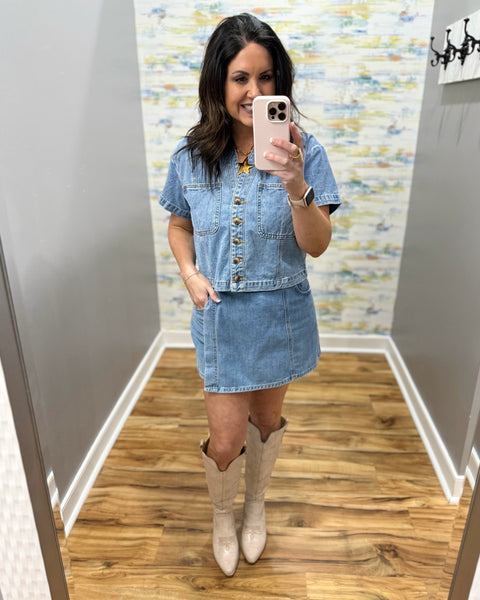 Woman wearing a denim skort and denim top with beige boots.