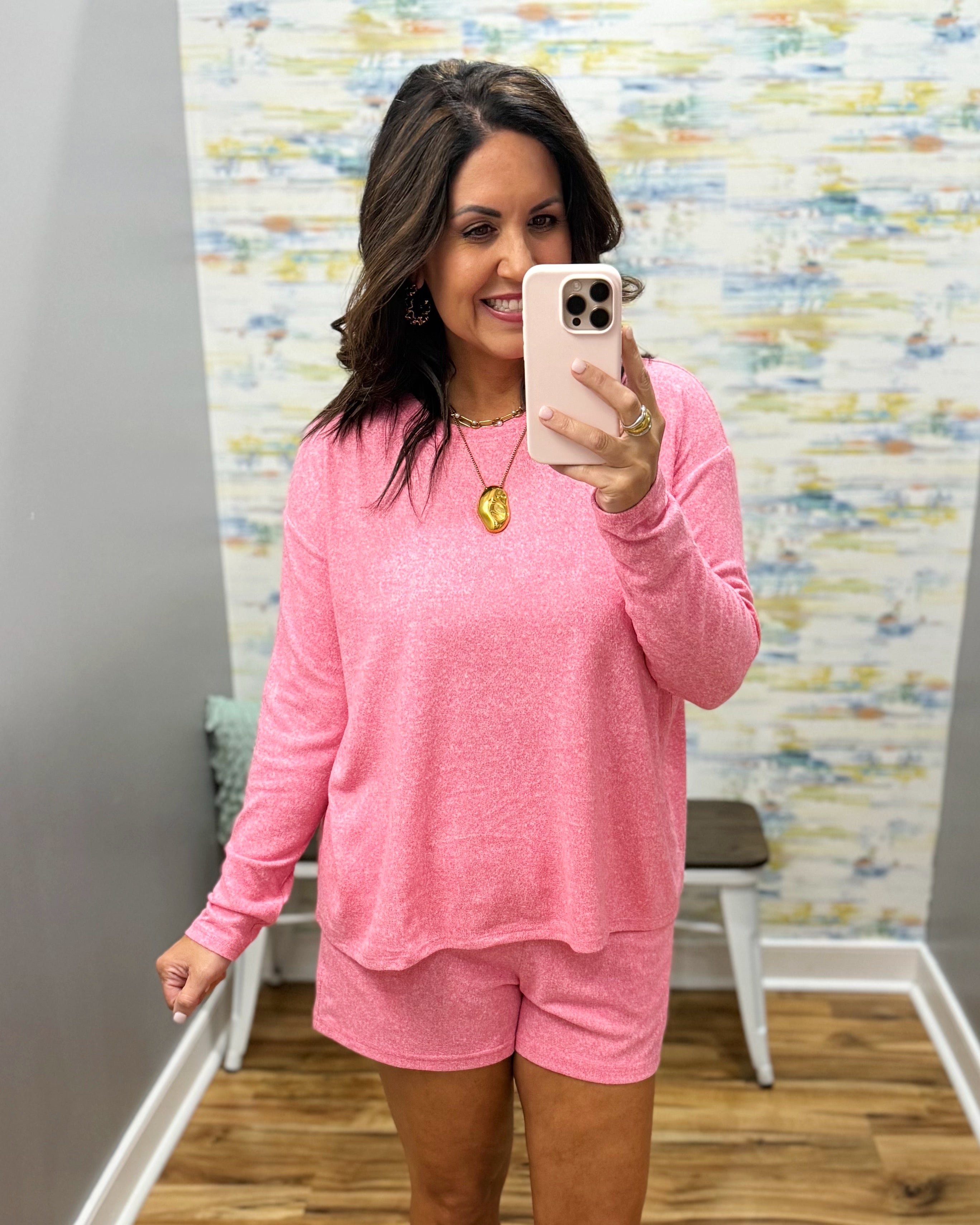 Woman taking a mirror selfie wearing a pink outfit in a room with a colorful wall.
