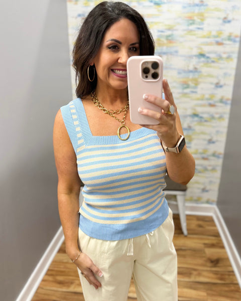 Woman wearing a blue and yellow striped sleeveless top and white pants.