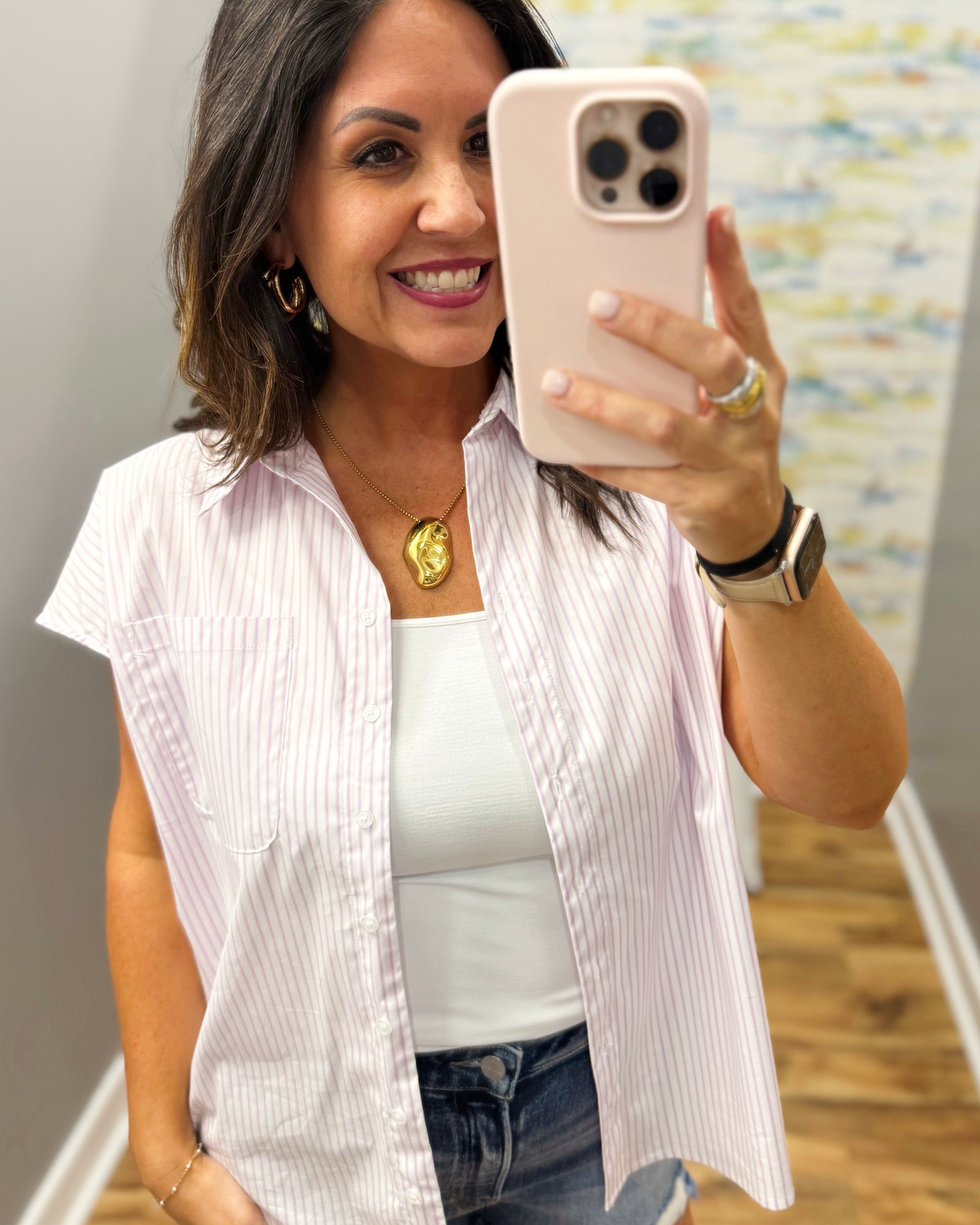 Woman taking a mirror selfie wearing a white shirt and blue jeans indoors.