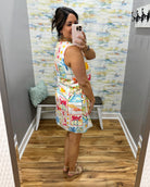 Woman taking a mirror selfie wearing a colorful dress in a room with a patterned wall.