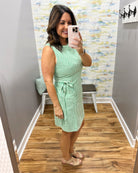 Woman taking a mirror selfie wearing a green dress in a room with a colorful wall.