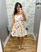 Woman wearing a floral dress in a fitting room with colorful wall and wooden floor.