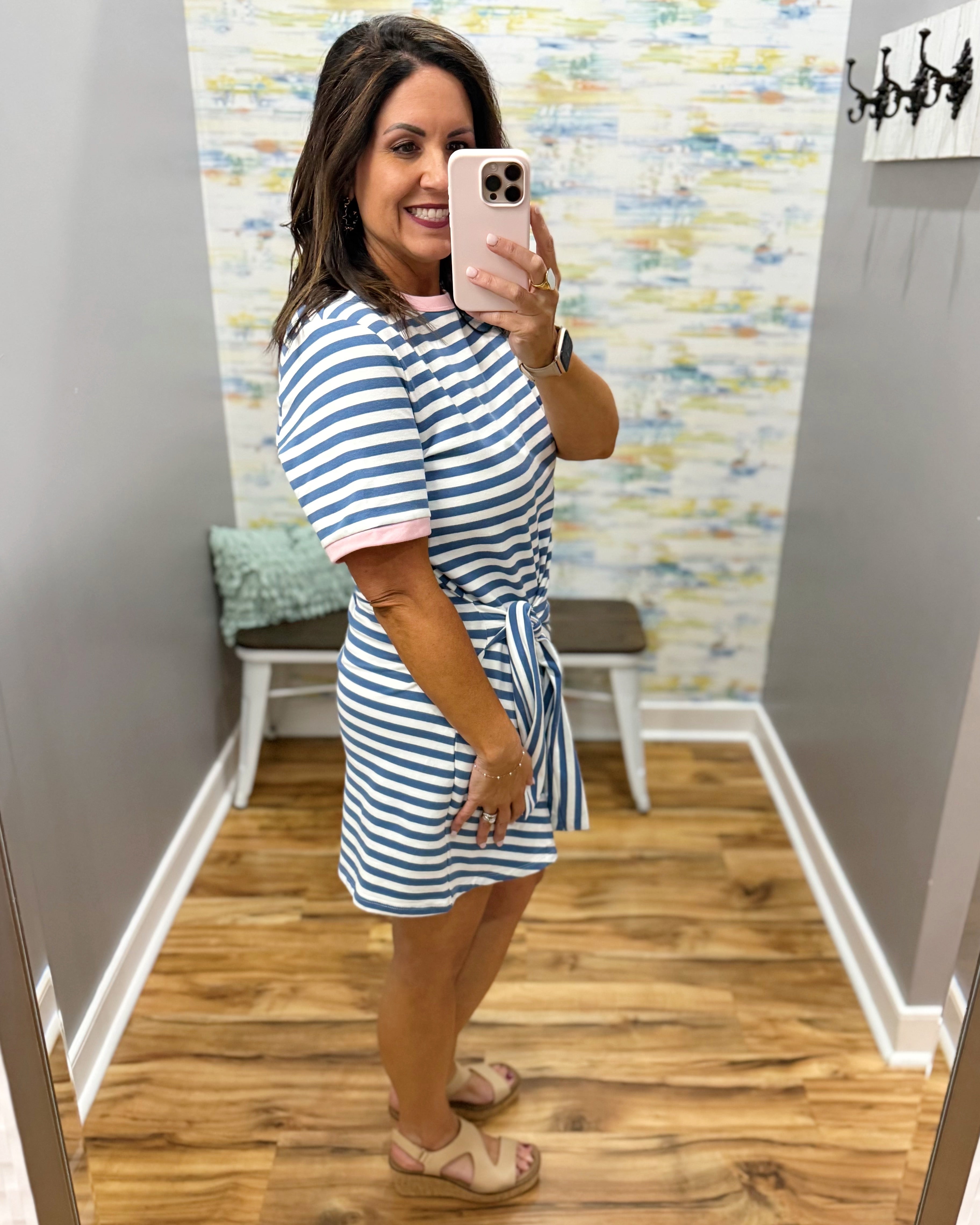 Woman taking a mirror selfie wearing a blue and white striped dress in a room with colorful wall art.