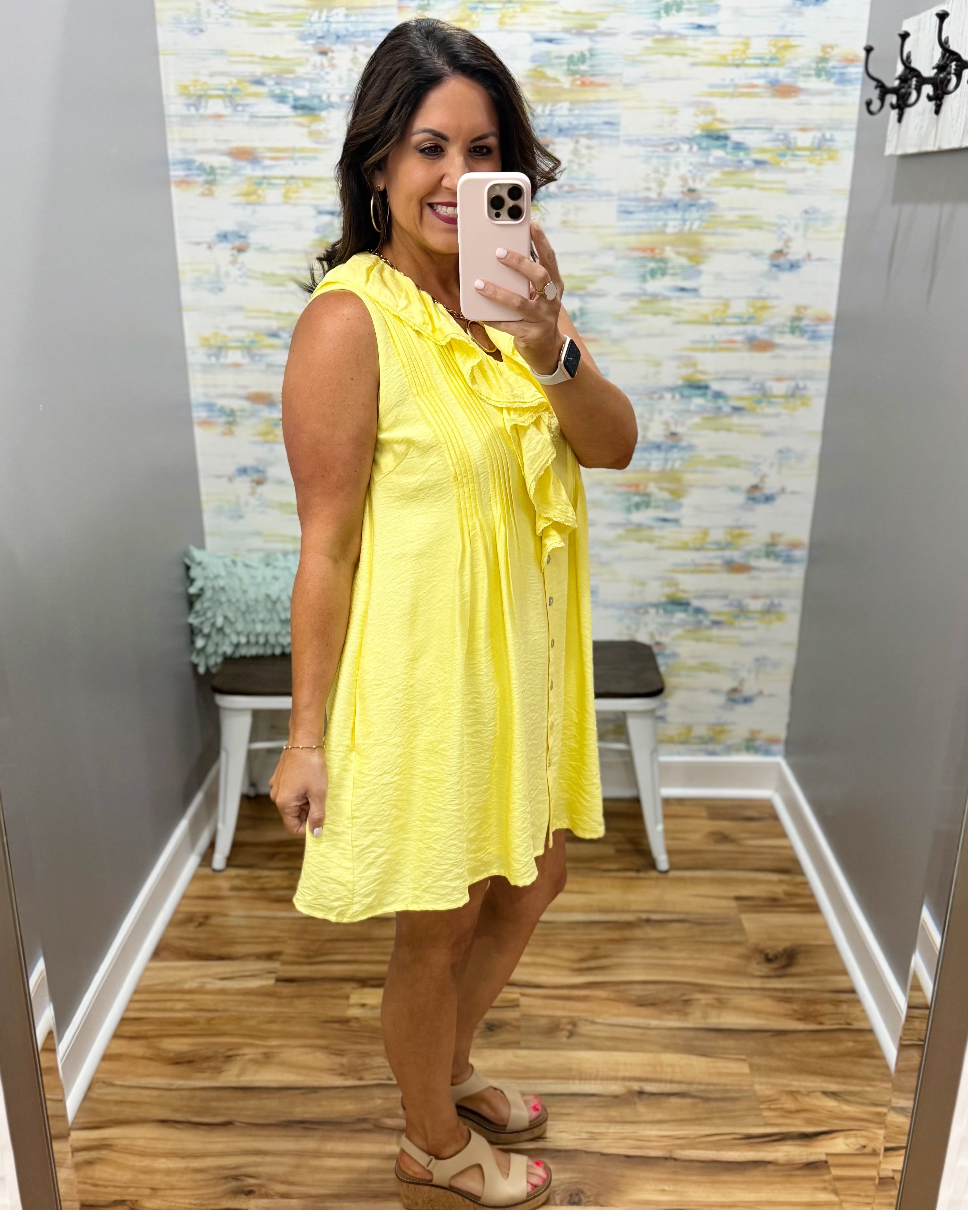 Woman taking a mirror selfie wearing a yellow dress in a room with patterned wallpaper.