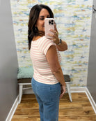 A woman taking a mirror selfie in a fitting room wearing a short-sleeve crewneck top with thin pink and white horizontal stripes, paired with blue jeans.