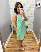 Woman taking a mirror selfie wearing a green and pink checkered dress in a room with a patterned wall.